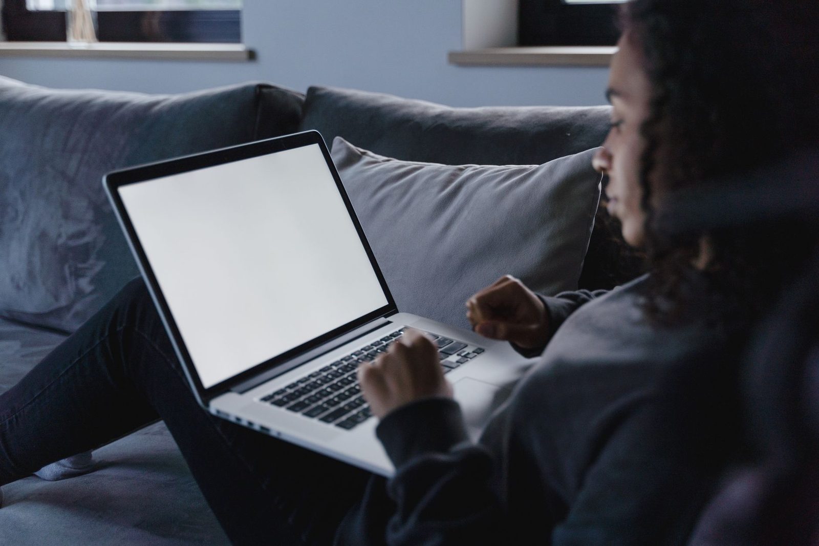 Young woman lying on a sofa using a laptop with a white screen