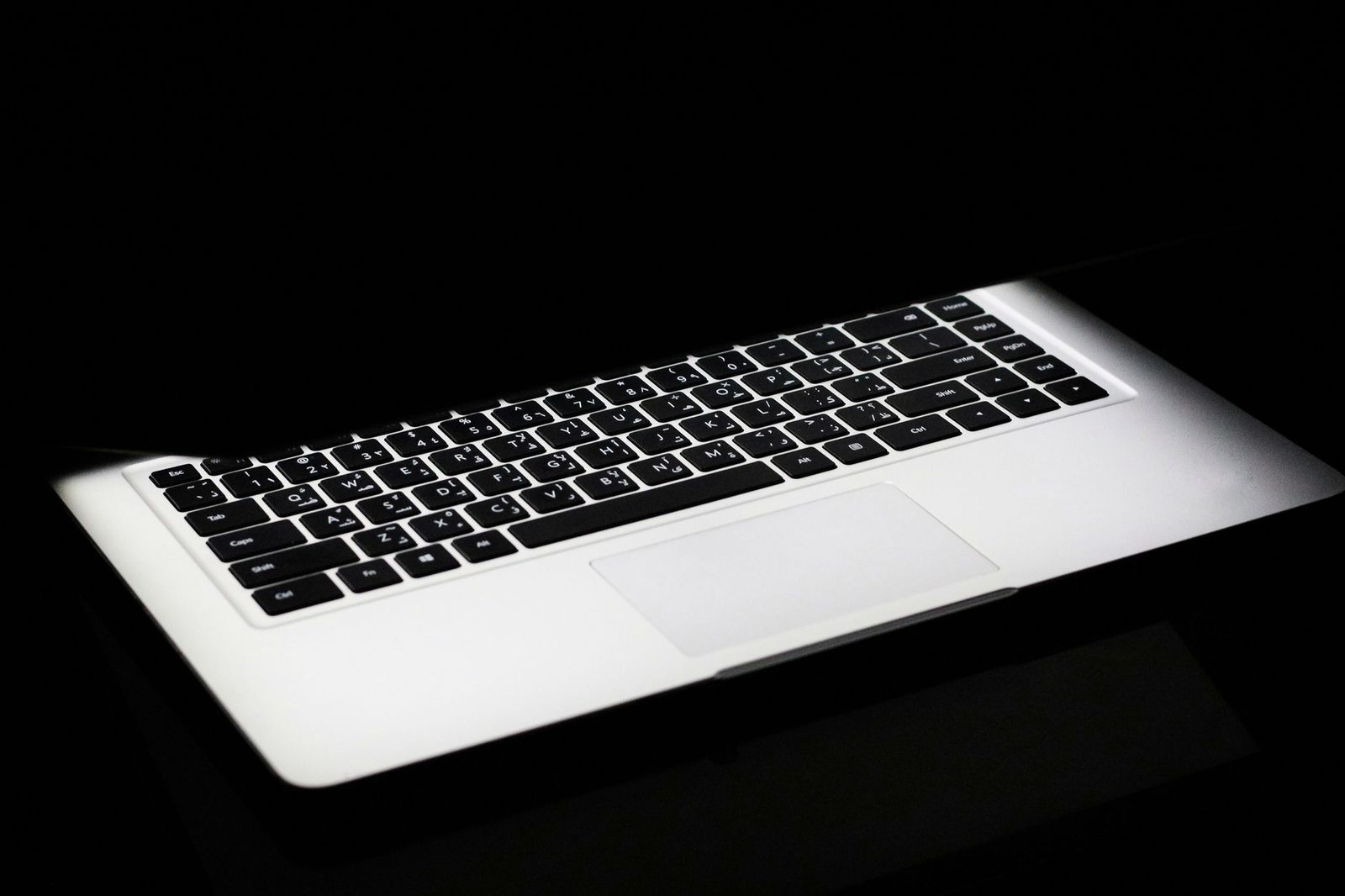 Open laptop lit up in the dark, keyboard and trackpad visible against a black background