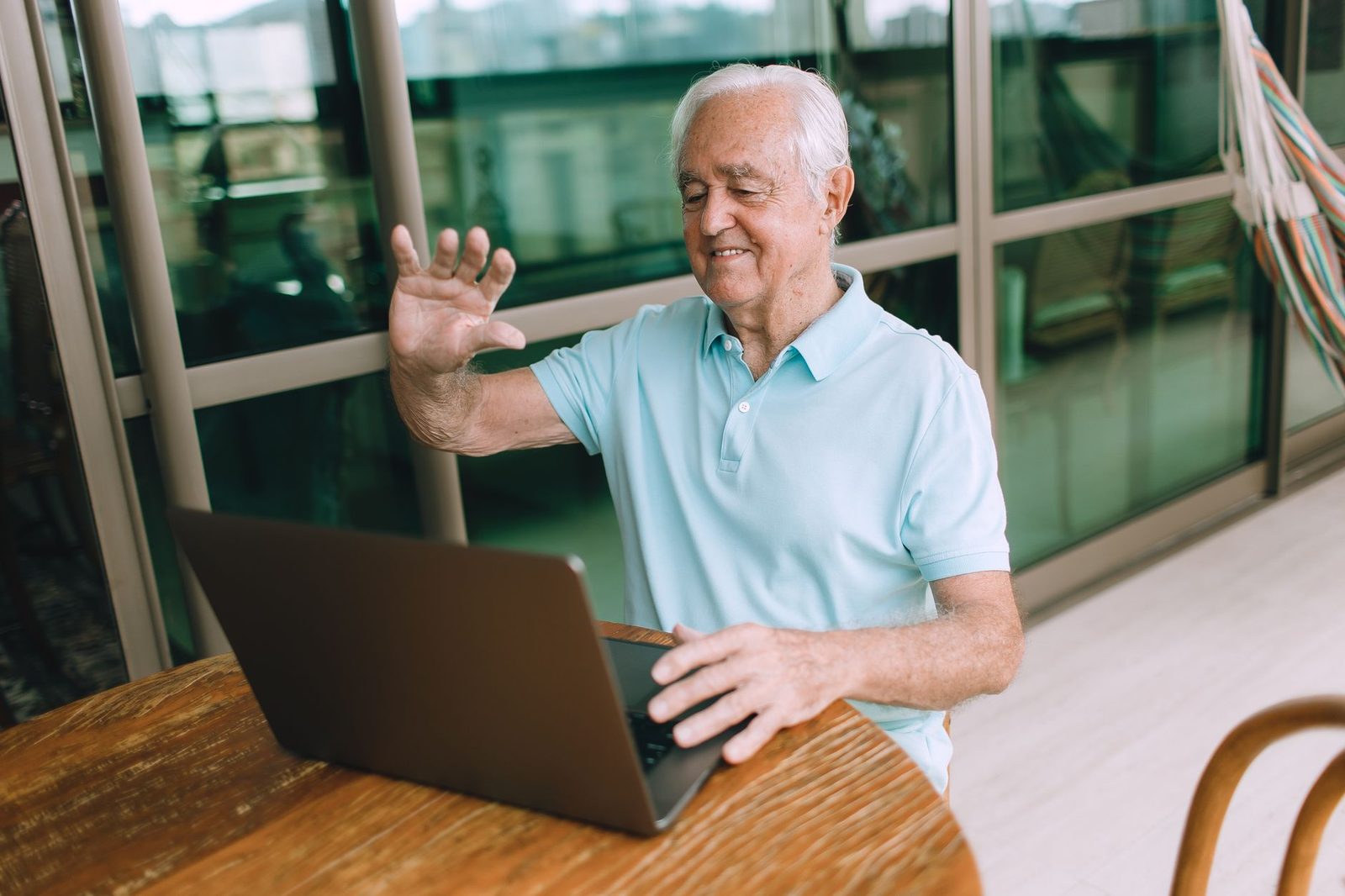 Uomo anziano sorridente che saluta con la mano davanti a un computer portatile durante una videochiamata