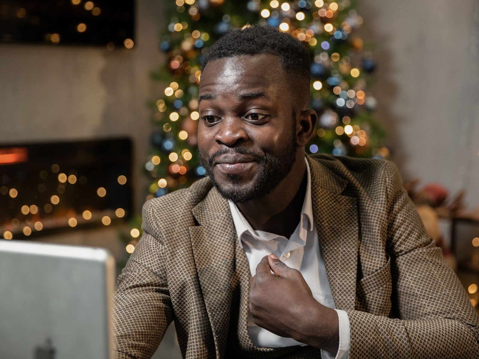 Homme en veste discutant devant un ordinateur portable, sapin de Noël lumineux en arrière-plan