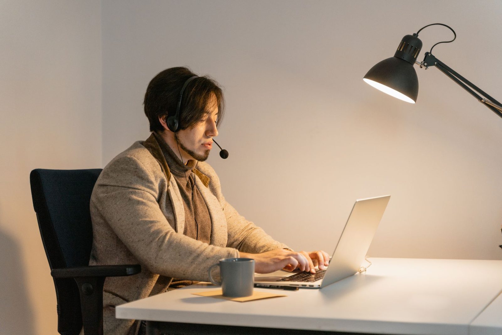 Homme avec casque-micro assis à un bureau, tapant sur un ordinateur portable éclairé par une lampe