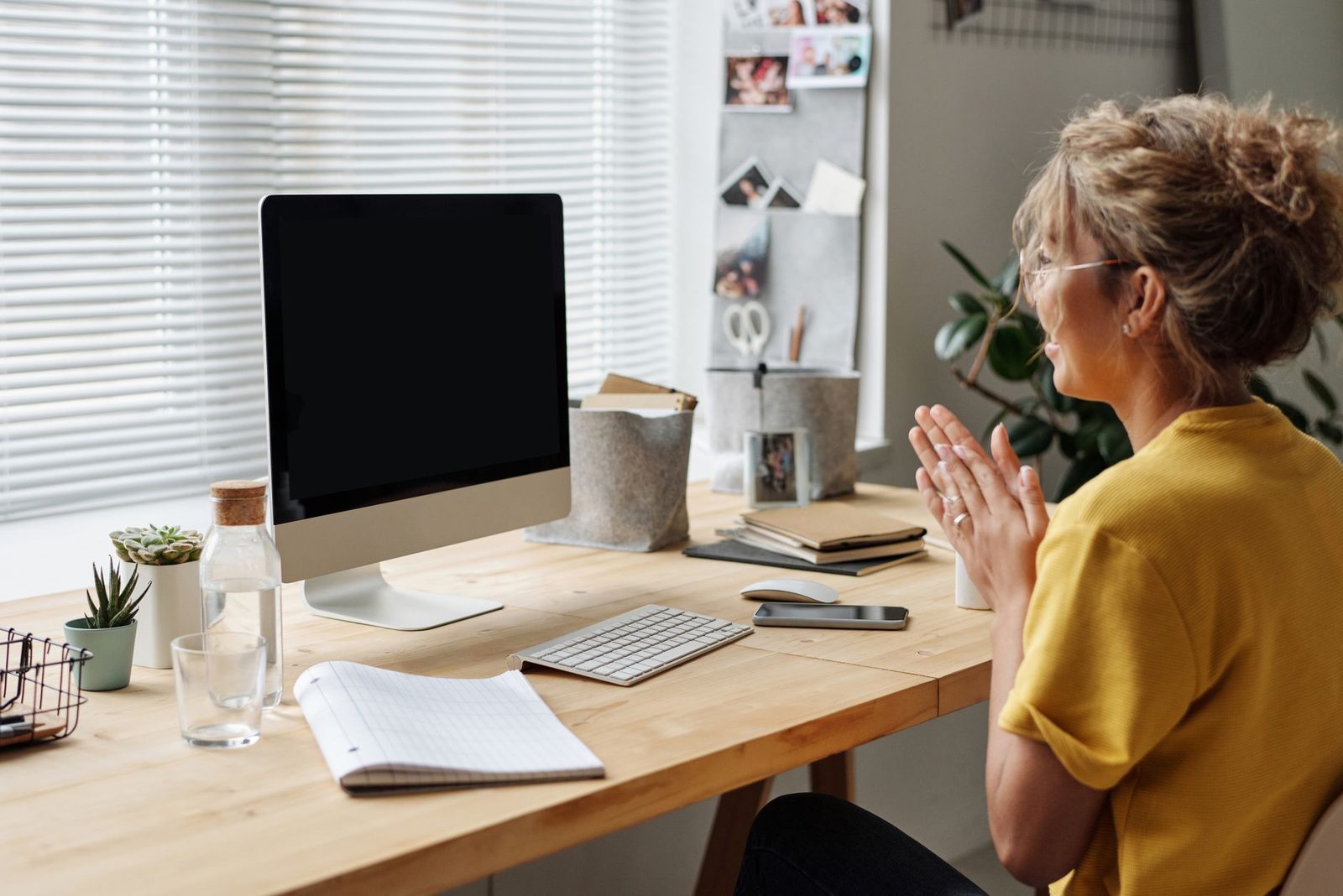 Smiling woman at a desktop computer, hands clasped, during a video conversation at home