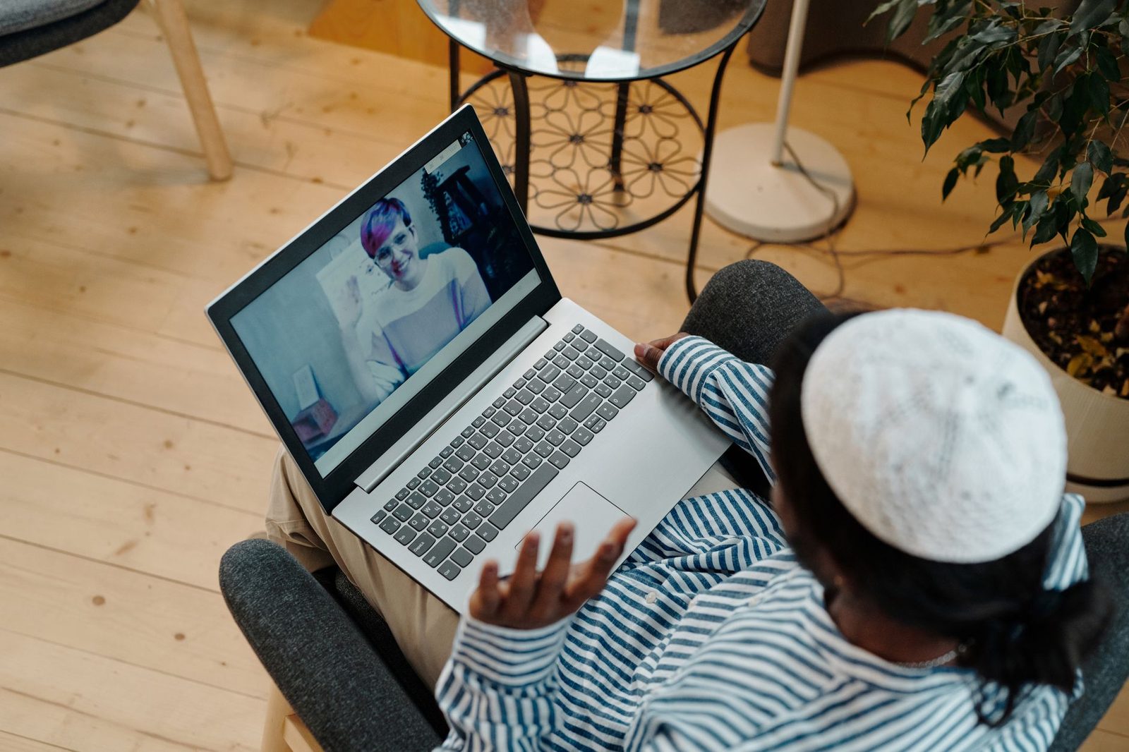 Woman sitting in an armchair chatting on a video call with a person shown on a laptop screen