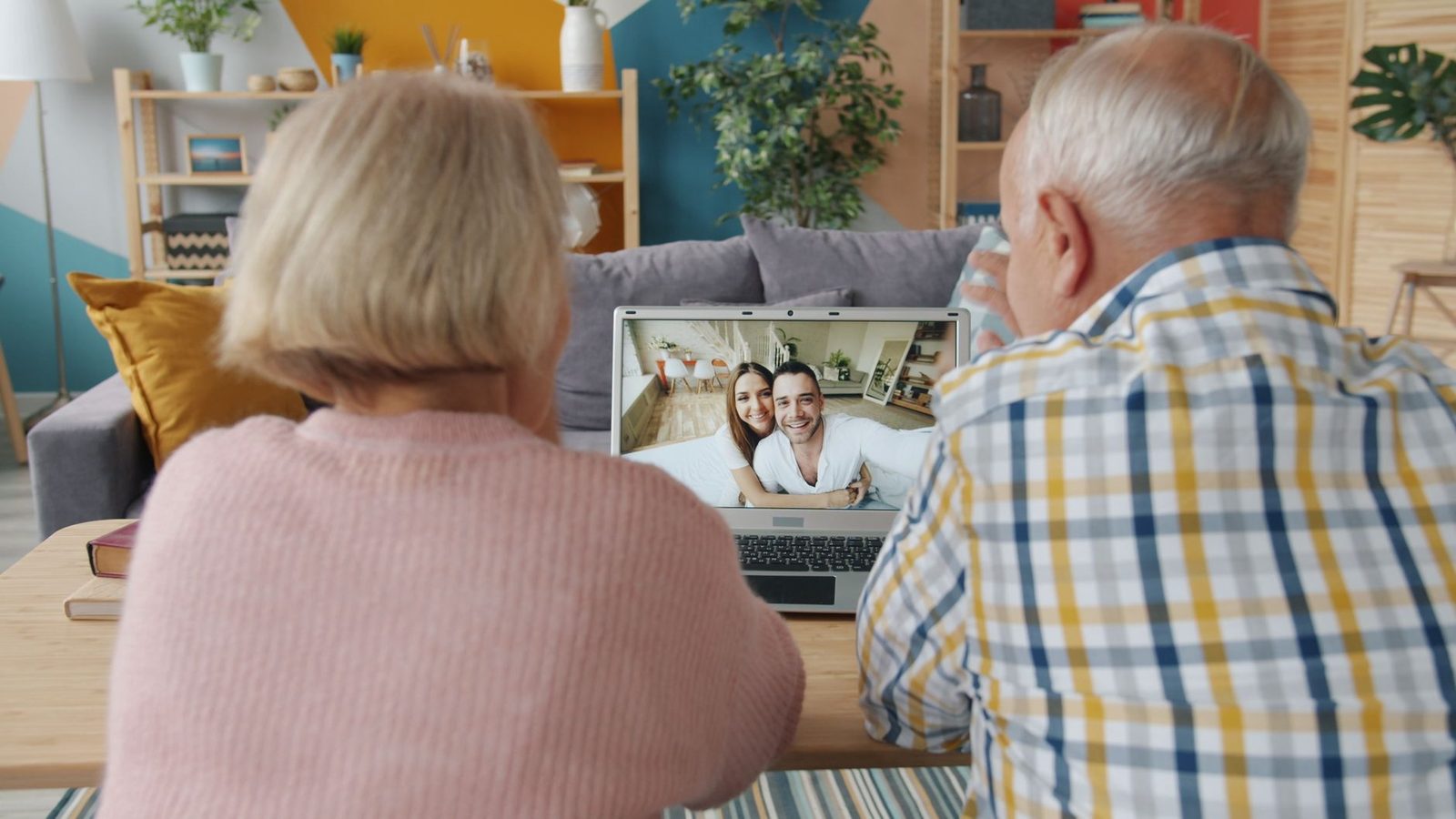 Elderly couple seen from behind on a video call on a laptop with a young couple on the screen