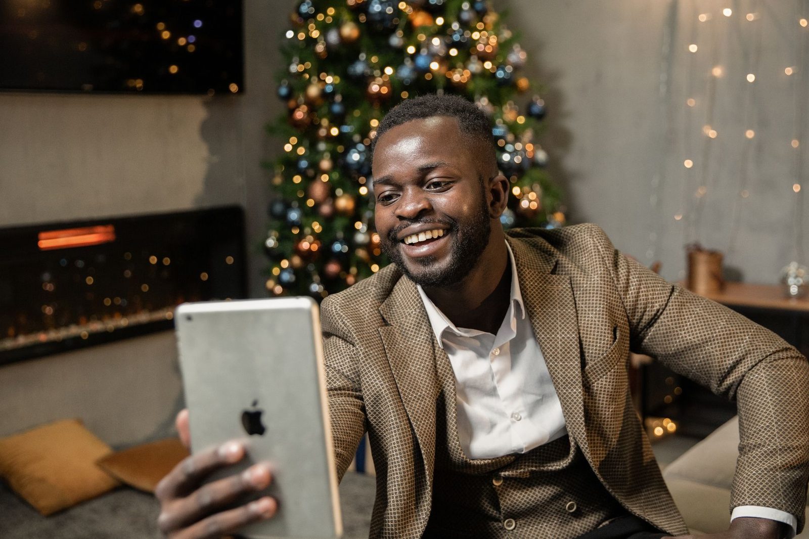 Homme souriant en costume passant un appel vidéo sur une tablette devant un sapin de Noël illuminé