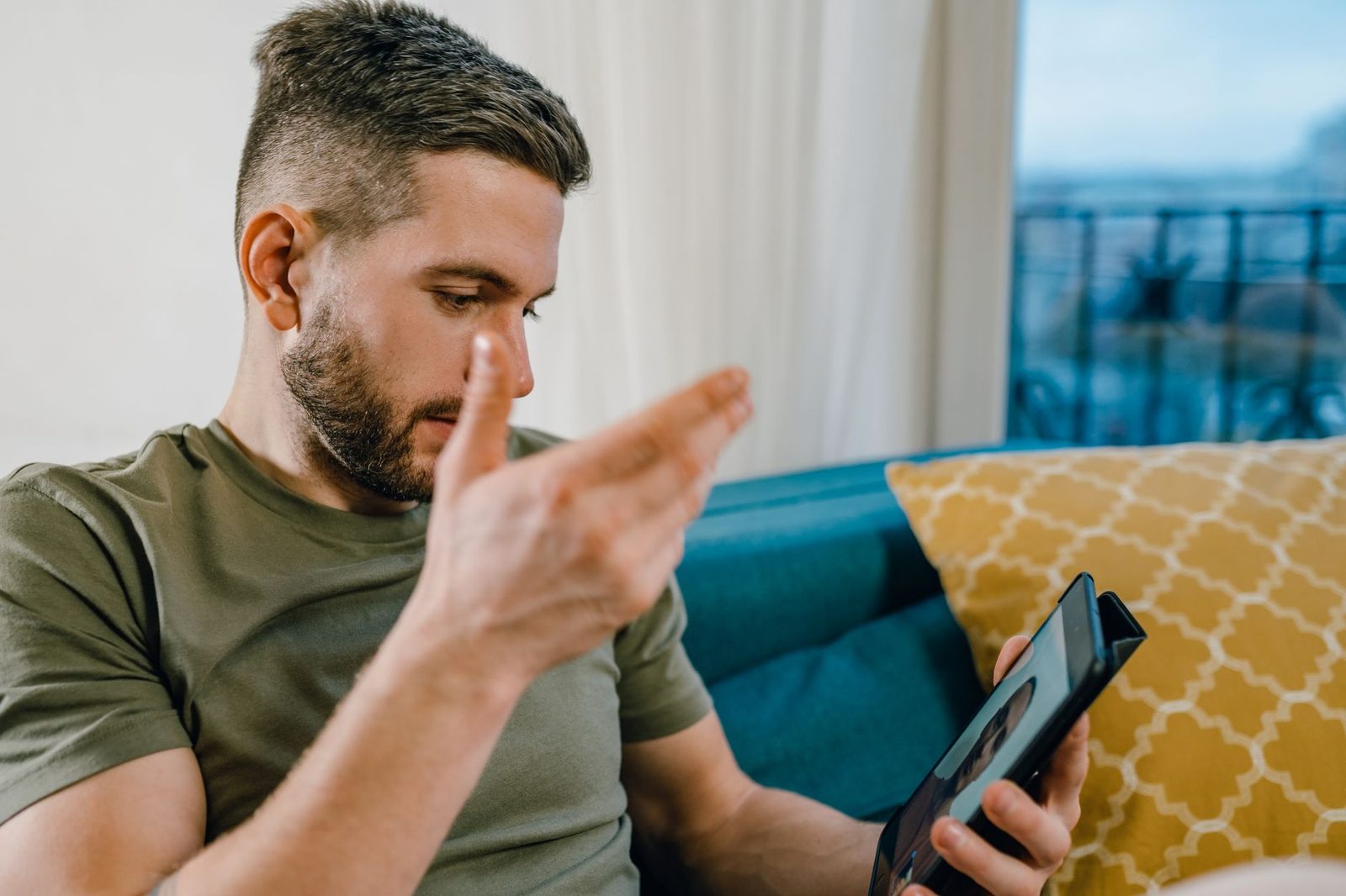 Homme assis sur un canapé faisant un signe de la main devant une tablette lors d'un appel vidéo