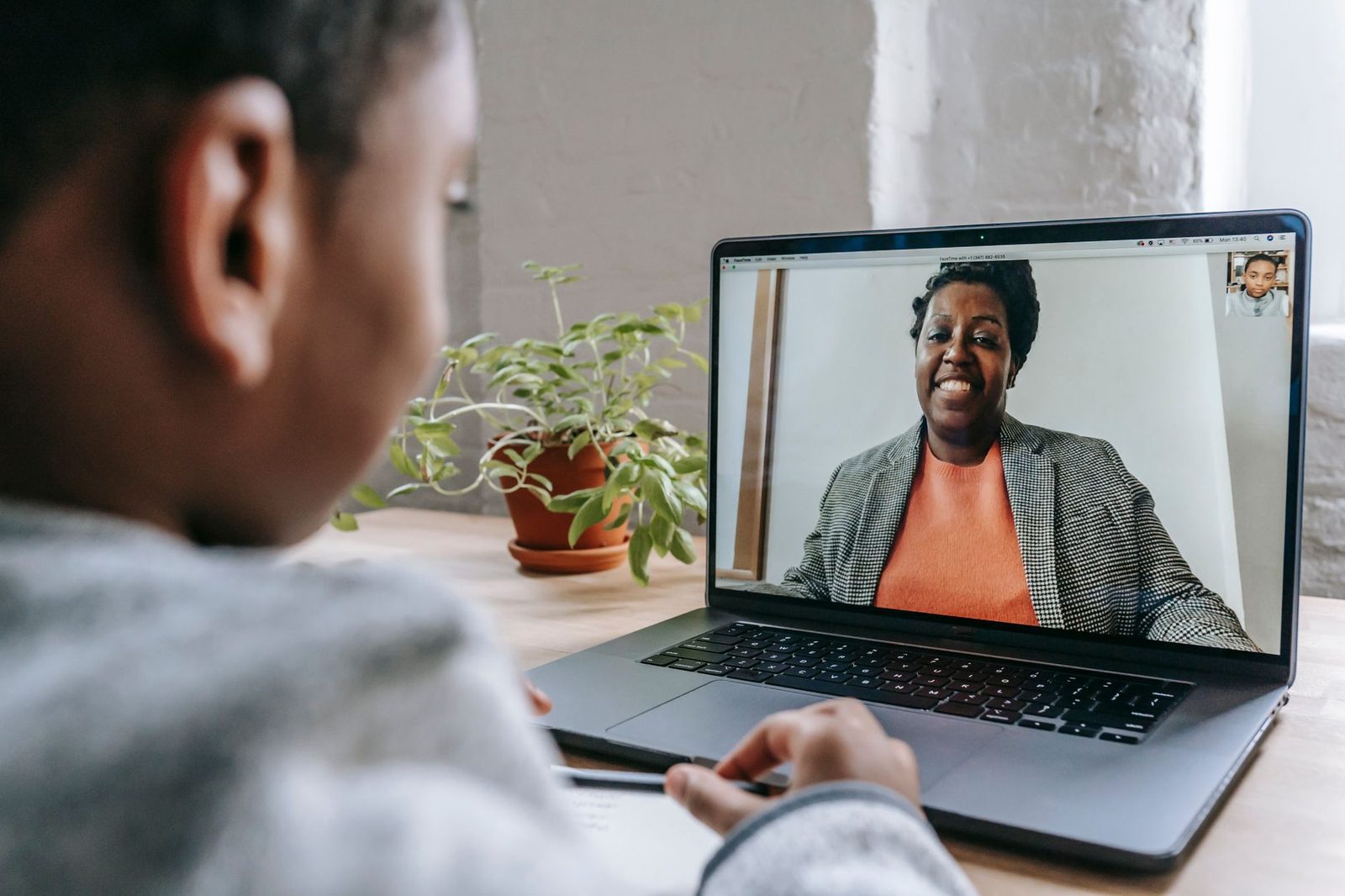 Une personne vue de dos regardant un appel vidéo sur un ordinateur portable avec une femme souriante à l'écran.